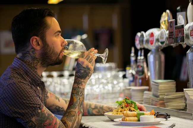 Tattooed man drinking wine and enjoying a meal at the bar at Cookie