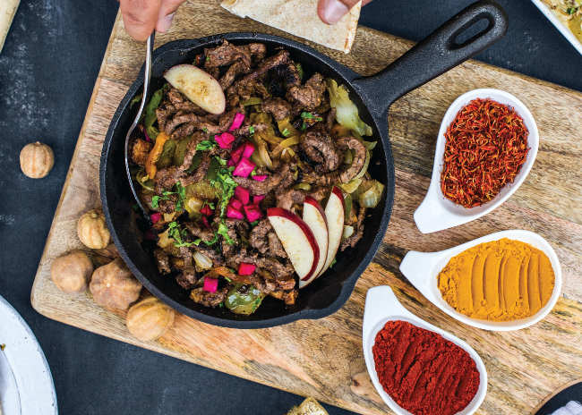 Chopping board filled with spices and frying pan filled with cooked meat and vegetables