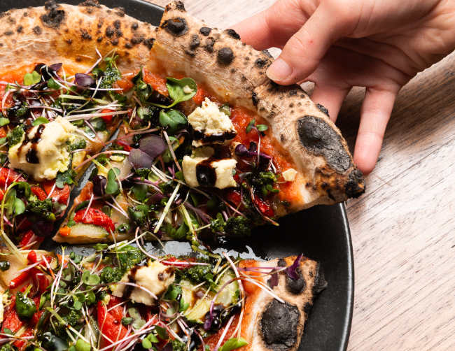 a hand grabbing a piece of vegan pizza