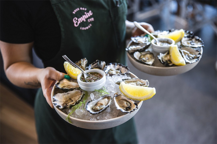 a waitress holding two plates of oysters at empire lounge restaurant