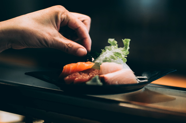 someone garnishing a plate of sushimi