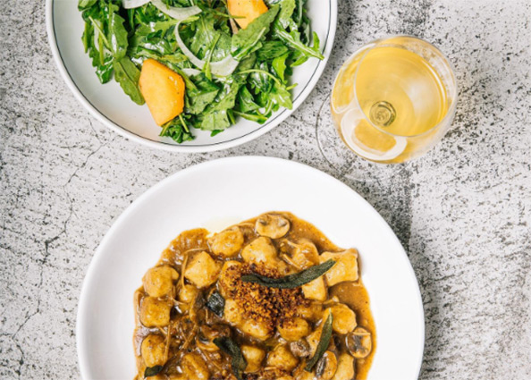 a pasta and sald bowl sitting next to a glass of wine