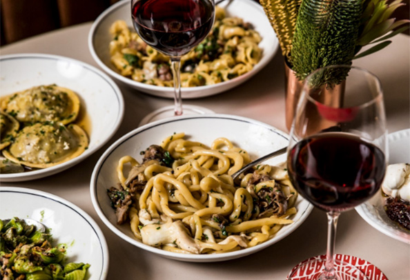 an assortment of pasta bowls and wine sitting on the table at a restaurant