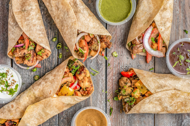 a table with five tasty burritos with dips
