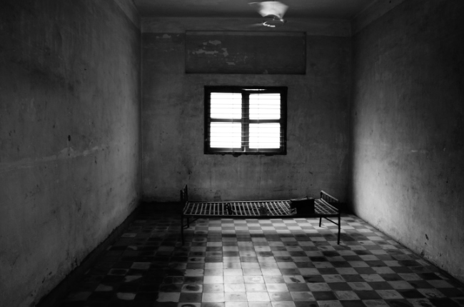 a dark prison cell with a bed in the middle of the room