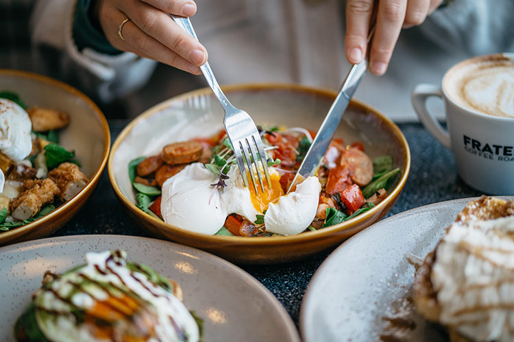 a close up of a lady eating brunch with 5 other meals on the table