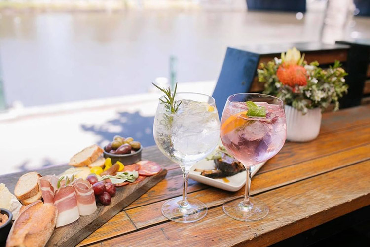 two cocktails sitting on the table with food at a restaurant