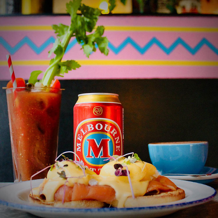 a close up photo of eggs bennedict and a can of VB alongside a bloody mary at a cafe in melbourne