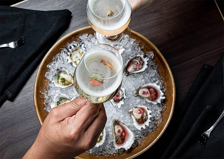 two people saying cheers with glasses of champange and oysters at riley st garage