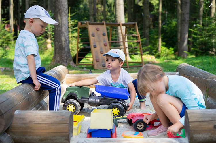 three kids playing outside in the sand with toys