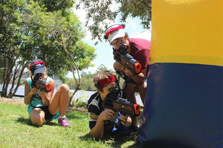 three people standing in a field holding up laser tag guns getting ready to shoot