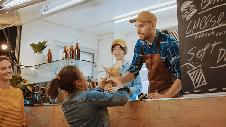 a man handing a woman a crepe in a food stall