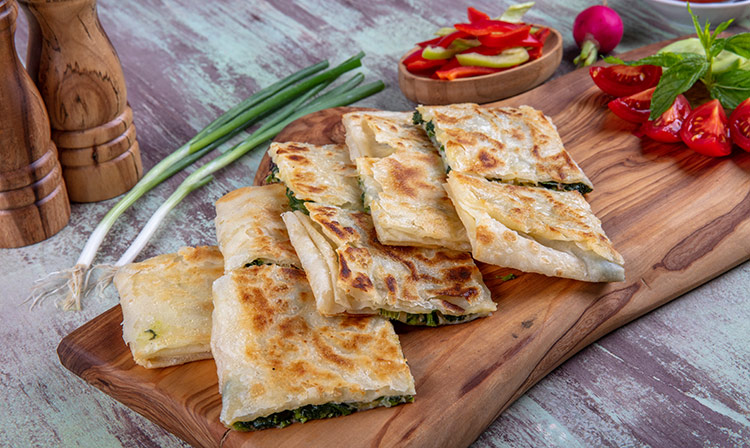 gozleme on a wooden board with vegetables on the side