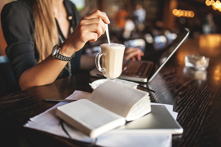 a woman twirling her coffee with a spoon while on her laptop at a cafe