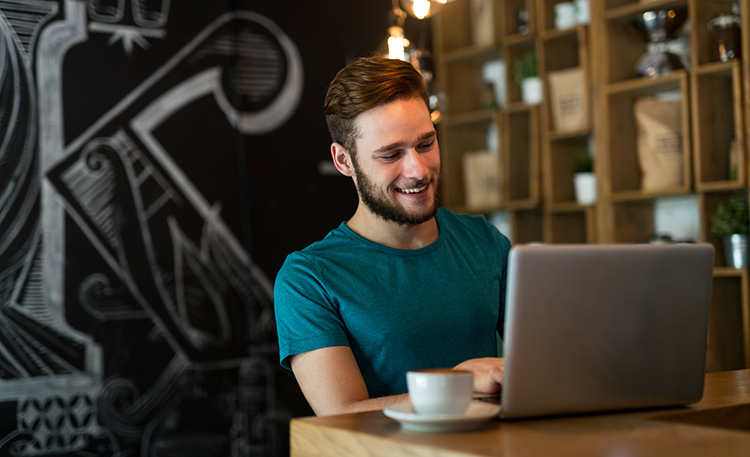 a man smiling at his laptop at a cafe