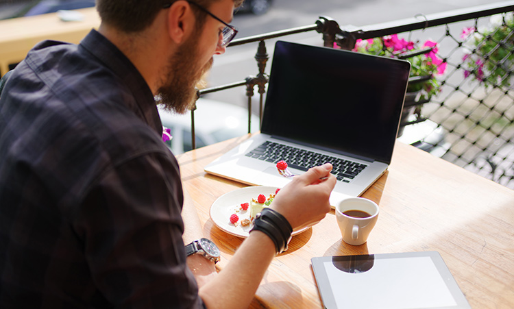 a man sitting down eating a cake with his laptop infront of him